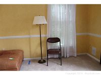 Floor lamp standing next to brown folding chair in a room with yellow walls and white curtains, showing full lamp and chair