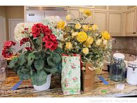 Three silk flower arrangements placed on kitchen counter including red geraniums, white hydrangeas, yellow roses, and a fabric bag of decorative pears.