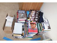 Photo of three large stacks of sports books and one box of autograph cards on floor, shows general assortment of lots