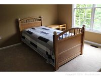 Side view of wood twin bed frame with patchwork quilt and white baseball finials on posts.