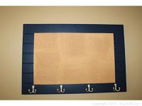 Front view showing the cork board framed in dark material with four metal double hooks along the bottom