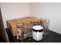 Photo showing a box of 12 mugs and glasses on a table, including a black and white Starbucks NYC mug, clear glass Guinness pint glass, and several other clear glass mugs with logos.