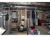 Full view of large metal sports cage with black netting enclosing snowboards and skis inside a basement storage area.