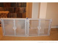 Photo showing 2 white plastic safety gate panels side by side against a wall, featuring lattice design and hinge connectors.