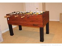 Full side view of the Twister II foosball table showing wood grain finish on cabinet, black legs, and wooden handles on chrome rods. Shows wear and tear.