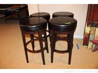 Four round wood and black leather barstools grouped together showing overall condition and design.