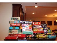 Photo showing a large variety of board game boxes stacked including Mindtrap, Battleship, Scrabble, Boggle, Blokus 3D, Tri-Ominos, Man Laws, Ghost, Scene It?, and others.