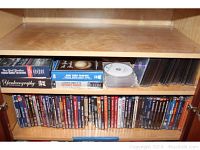 DVD collection stored on wooden cabinet shelves; includes titled DVDs and some bare discs