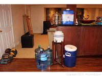 Photo showing all items including three 5-gallon water jugs, ceramic water jug on a wooden stand, blue Igloo water dispenser, and blue Aqua Tainer jug on a raised surface.