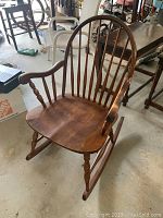Full view of a vintage walnut rocking chair with spindle back, rounded armrests, and turned legs on rockers.