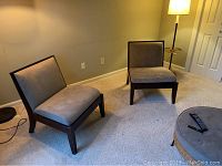 Two Crate and Barrel slipper chairs with gray upholstery and dark wooden frames arranged in room on light carpet near floor lamp.