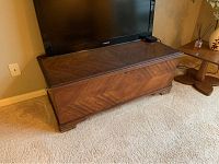 Front and side view of wood cedar chest with walnut veneer and geometric pattern on lid, placed on carpet with TV and table nearby.