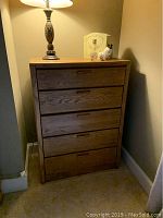 Front view of a wooden 4-drawer dresser placed in a corner with a lamp and decorative items on top.