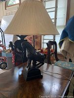 Photo showing vintage 1950s horse table lamp on wooden table with pleated beige lampshade and black horse base.
