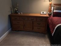 Wooden dresser with five drawers, a central cabinet door, and decorative handles, positioned beside the bed.