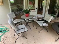 View of four black iron outdoor chairs with white striped cushions surrounding a round iron table with decorative top.