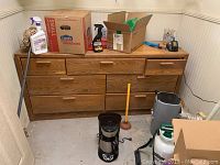 Photo showing a medium brown wooden dresser with seven drawers and various items placed on top and around it.