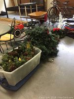 View of plastic bins filled with artificial pine greenery, pinecones, and clusters of red berries alongside other garage items.