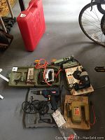 Lot of various electric tools including drills and jigsaws laid on floor near a bicycle and red toolbox