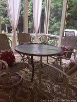 Round glass top table with textured glass and surrounding patio chairs on outdoor rug in screened porch.