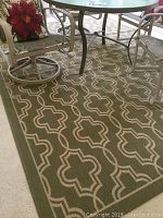 Full view of green and tan geometric patterned outdoor rug under patio table and chairs.