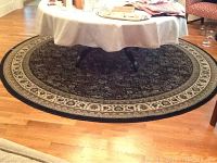 Full view of the round area rug under a table on hardwood floor, showing pattern and condition.