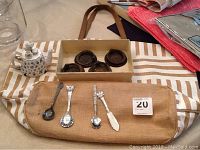 Photo showing Portmeirion ceramic teapot decorated with floral pattern and miniature tea set on lid beside several collectible spoons and brown metal door knockers on striped cloth.
