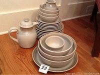 Stacked Noritake Painted Desert stoneware plates, bowls, cups including a teapot on the left side, arranged on hardwood floor.