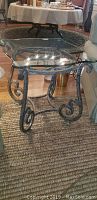 Side view of the Thomasville Grandview end table showing metal scroll base and glass top on woven rug.