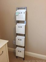 Full view of the Pottery Barn Teen 4 pocket metal wall organizer standing upright against a beige wall.