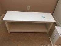 Front angled view of the white bench showing top surface and shelf underneath.