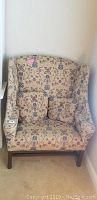 Front view of the oversized high-back upholstered chair featuring floral and geometric upholstery, with two matching throw pillows, positioned next to a window.
