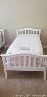 Full view of white twin bed frame with mattress on top, showing headboard and footboard with slats.