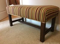 Side angled view of fabric cover bench showing striped upholstery and wooden legs with cross supports.
