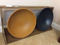 Rectangular wooden shelf holding two wooden bowls, one yellow and one navy blue, sitting on carpeted floor