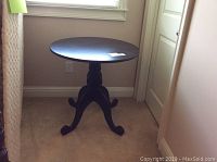 Side view of the black round pedestal table showing the curved legs base and circular tabletop.