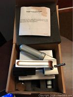 View of opened box containing Pungo Argon Cartridge Wine Dispenser device and instruction manual laid on foam padding.