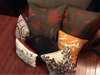 Front view of 7 throw pillows arranged, showing variety of patterns and sizes, including two large brown floor pillows with red coral design and five smaller decorative pillows.