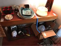 Front view of the Crate and Barrel Aldo console table with various items on top and beneath it, showing wood finish and scratches.