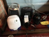 Four fan heaters and one mini dehumidifier placed on the floor, showing size and appearance of each with cords visible.