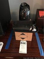 Braun Series 2 electric shaver standing in charging cradle with black travel case open and placed in front on cardboard box, showing entire lot.