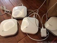 Four eero units on hardwood floor with cables