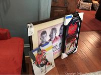 Framed 'Young Guns' poster alongside the framed Matt Niskanen jersey piece with unframed photograph of Ovechkin on floor near red chair and cabinet.