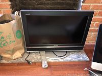 Sony Bravia 26 inch television with remote control placed on a marble slab against a brick fireplace background.