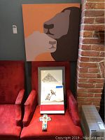 Full view of large painting of two bears above two framed artworks on chair, with decorative wooden cross in front