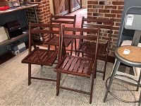 Four dark brown wooden folding chairs arranged together with visible slatted seat and backrest.