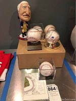 Overview photo showing five signed baseballs encased in display holders and a George Washington bobblehead figurine in colonial outfit. A paper listing names of players who signed one of the balls is included.