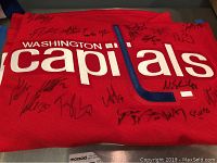 Folded red Capitals jersey front showing “Washington Capitals” wordmark and multiple black-ink signatures