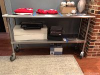 Full frontal view of the stainless steel serving cart with wheels, showing the top and lower shelves and items placed on it.