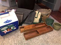 Full view of lot items including Playmate Igloo cooler, two small planter pots, two woven baskets, walnut trays, leather portfolio, Jack Spade bag, and picnic bag.